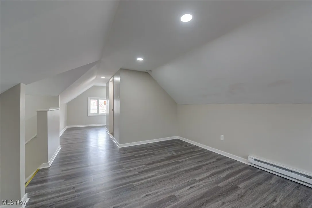 Additional living space with dark wood-style floors, recessed lighting, lofted ceiling, and baseboard heating