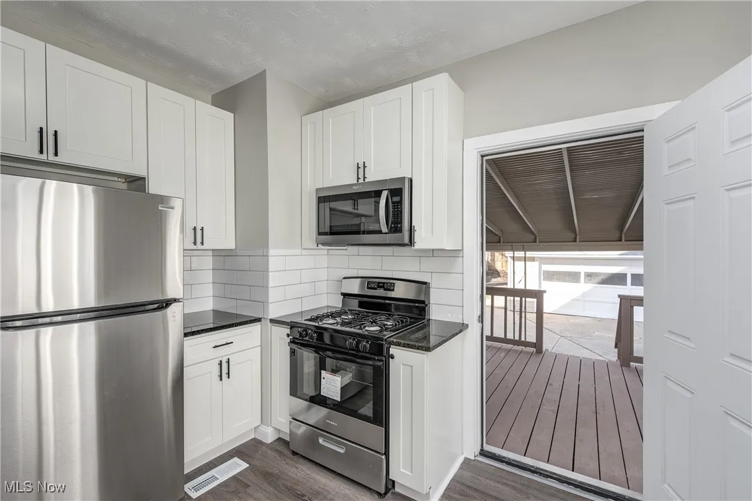 Kitchen featuring stainless steel appliances, white cabinetry, dark stone countertops, and decorative backsplash