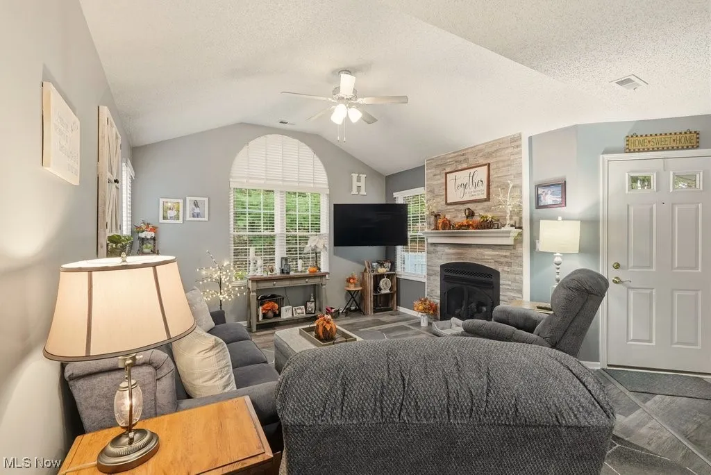 Living room featuring a fireplace, lofted ceiling, a textured ceiling, and a ceiling fan