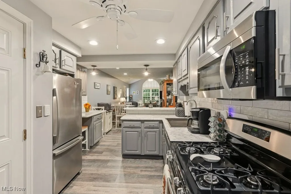 Kitchen featuring appliances with stainless steel finishes, gray cabinets, open floor plan, light wood-style flooring, and tasteful backsplash