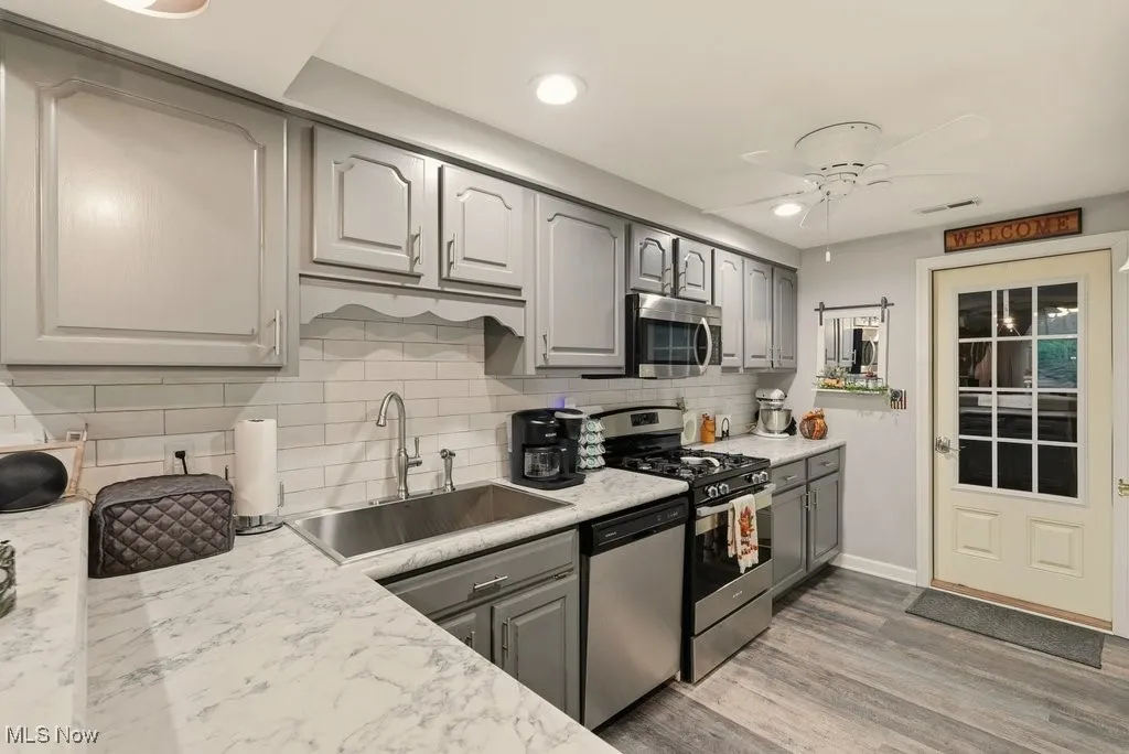 Kitchen featuring gray cabinetry, appliances with stainless steel finishes, decorative backsplash, wood finished floors, and a ceiling fan