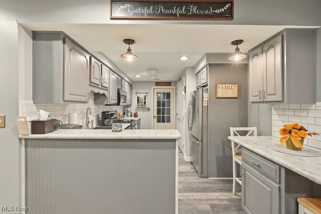 Kitchen with decorative backsplash, gray cabinetry, stainless steel appliances, recessed lighting, and light stone countertops