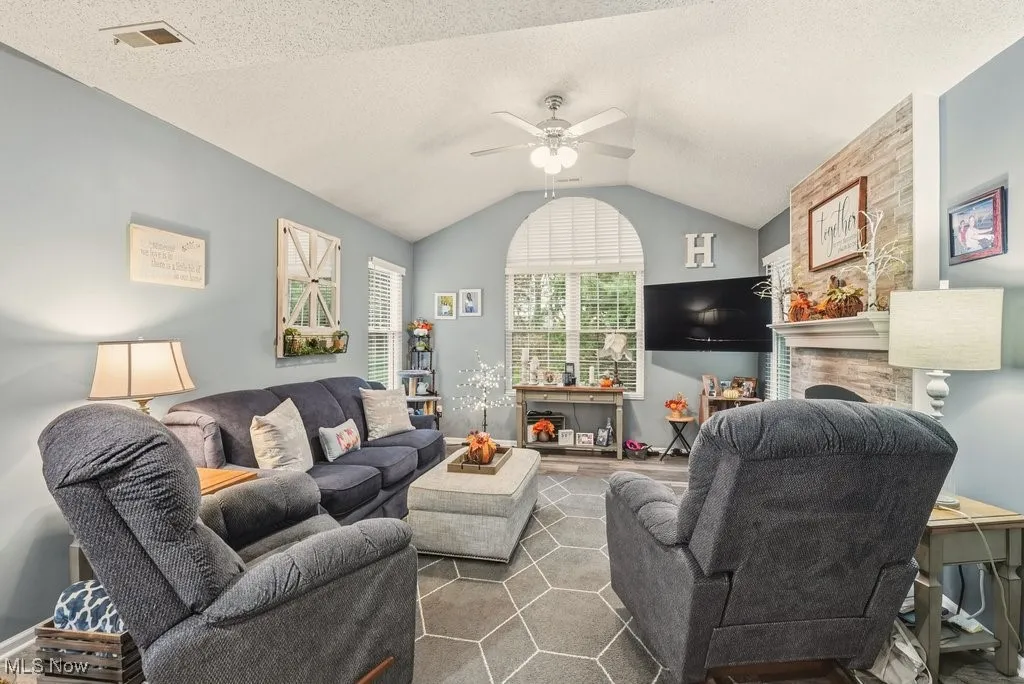 Living area featuring a ceiling fan, vaulted ceiling, a large fireplace, and a textured ceiling