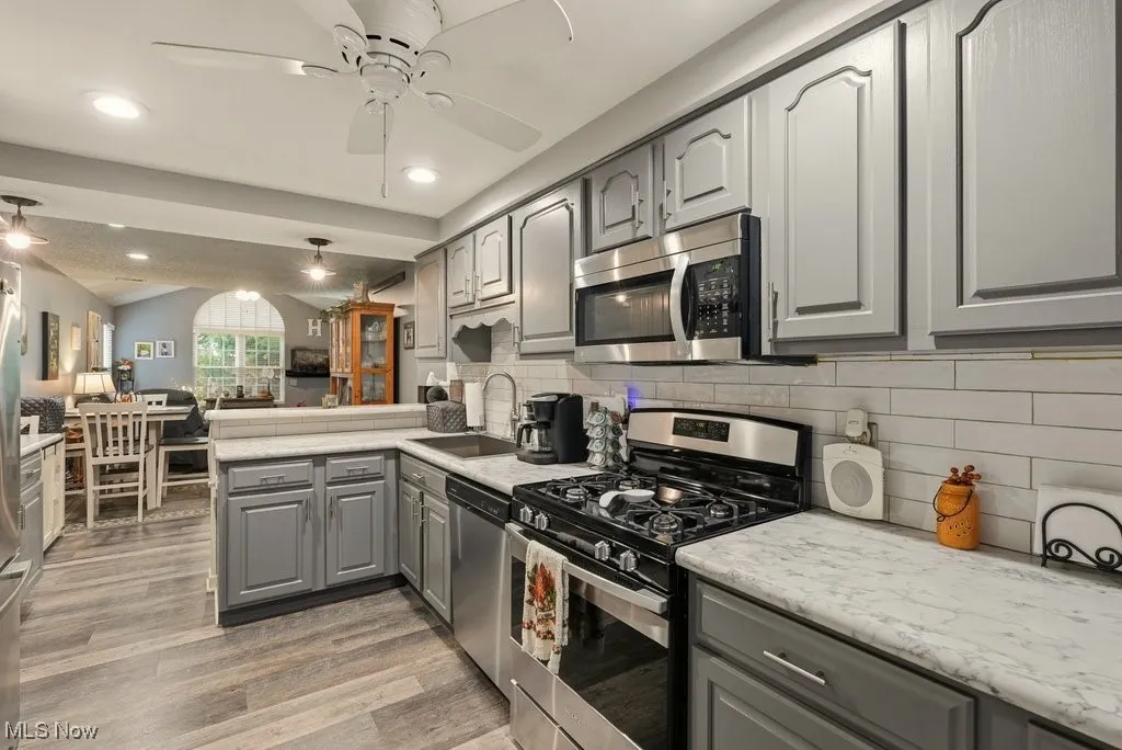 Kitchen with gray cabinets, stainless steel appliances, open floor plan, vaulted ceiling, and light wood-type flooring