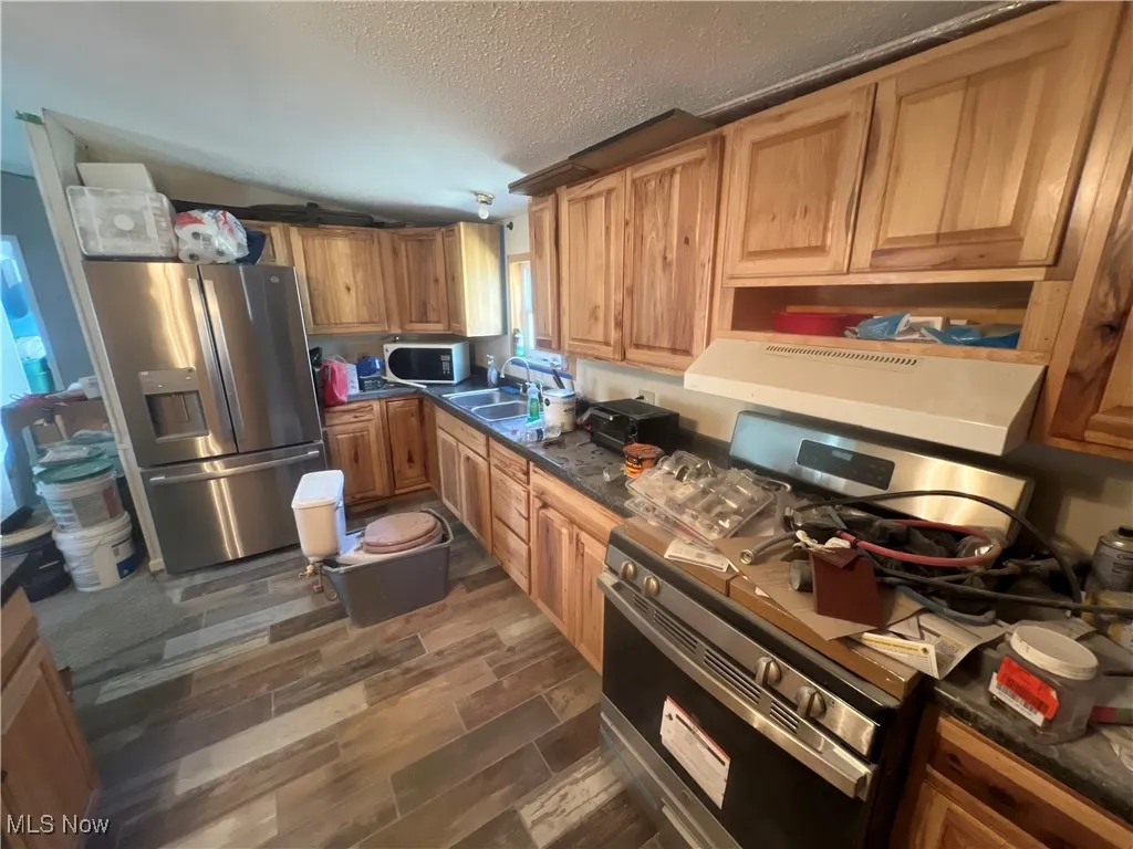 Kitchen with stainless steel appliances, a textured ceiling, wood tiled floors, extractor fan, and dark stone countertops