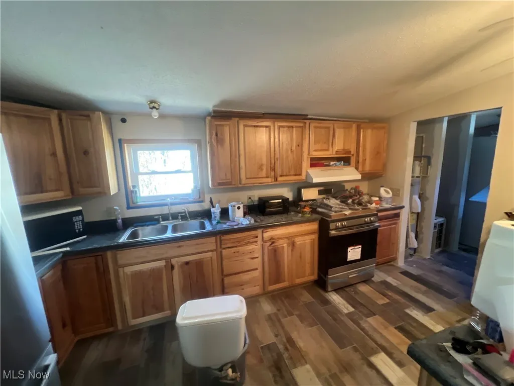 Kitchen featuring appliances with stainless steel finishes, dark countertops, dark wood finished floors, brown cabinets, and a textured ceiling