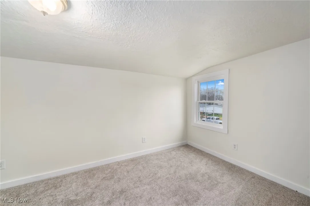 Unfurnished room featuring a textured ceiling, vaulted ceiling, and carpet floors