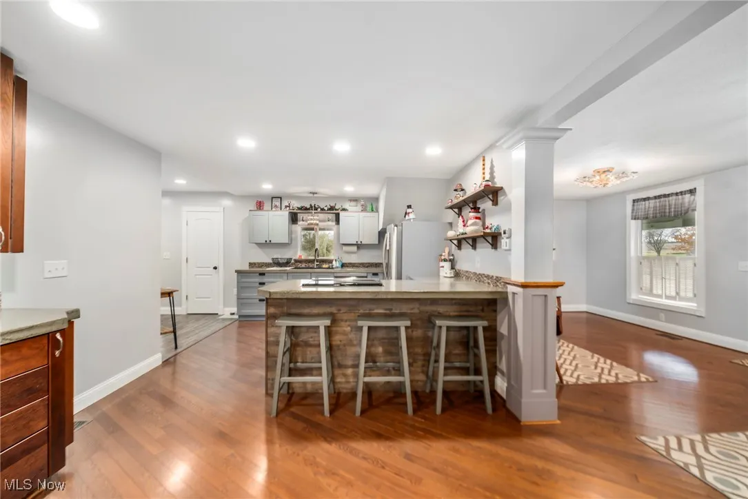 Kitchen featuring open shelves, dark wood finished floors, freestanding refrigerator, a peninsula, and a breakfast bar