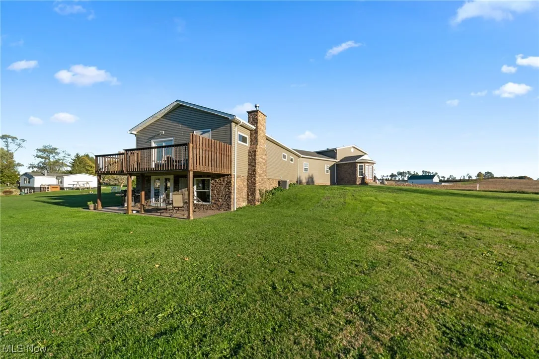 Rear view of house featuring a chimney, a yard, a patio, and a wooden deck
