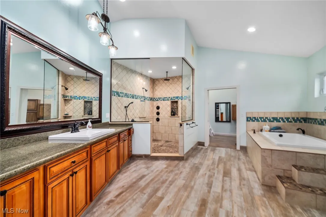 Bathroom with walk in shower, vanity, light wood-style flooring, a garden tub, and vaulted ceiling
