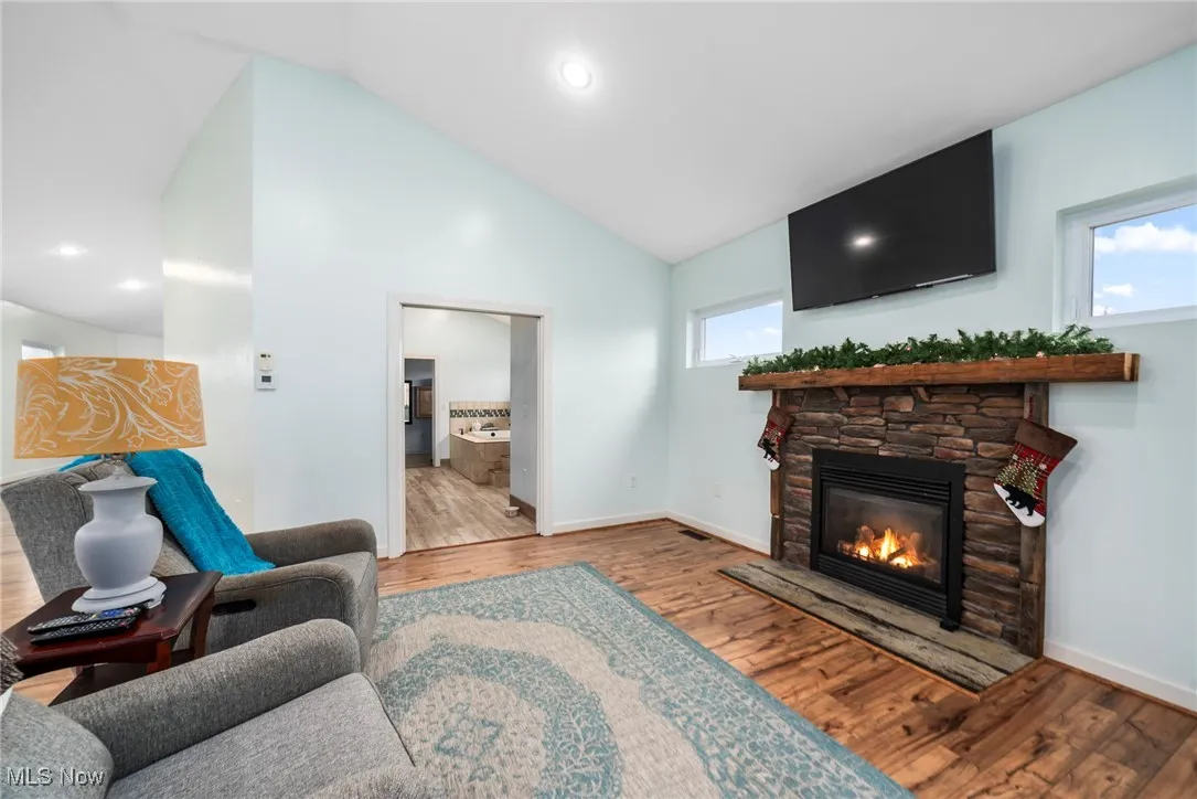 Living room featuring a stone fireplace, wood finished floors, high vaulted ceiling, and recessed lighting