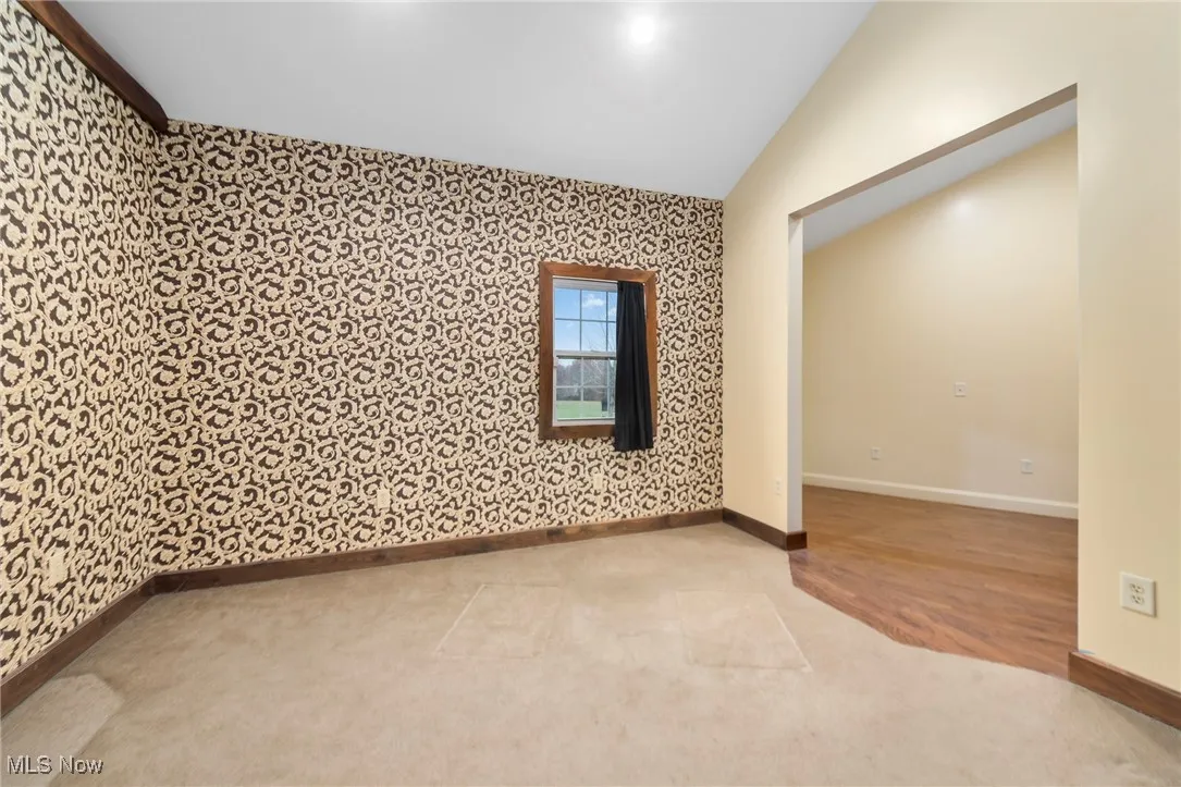 Unfurnished room featuring wallpapered walls, an accent wall, vaulted ceiling, and light wood-type flooring