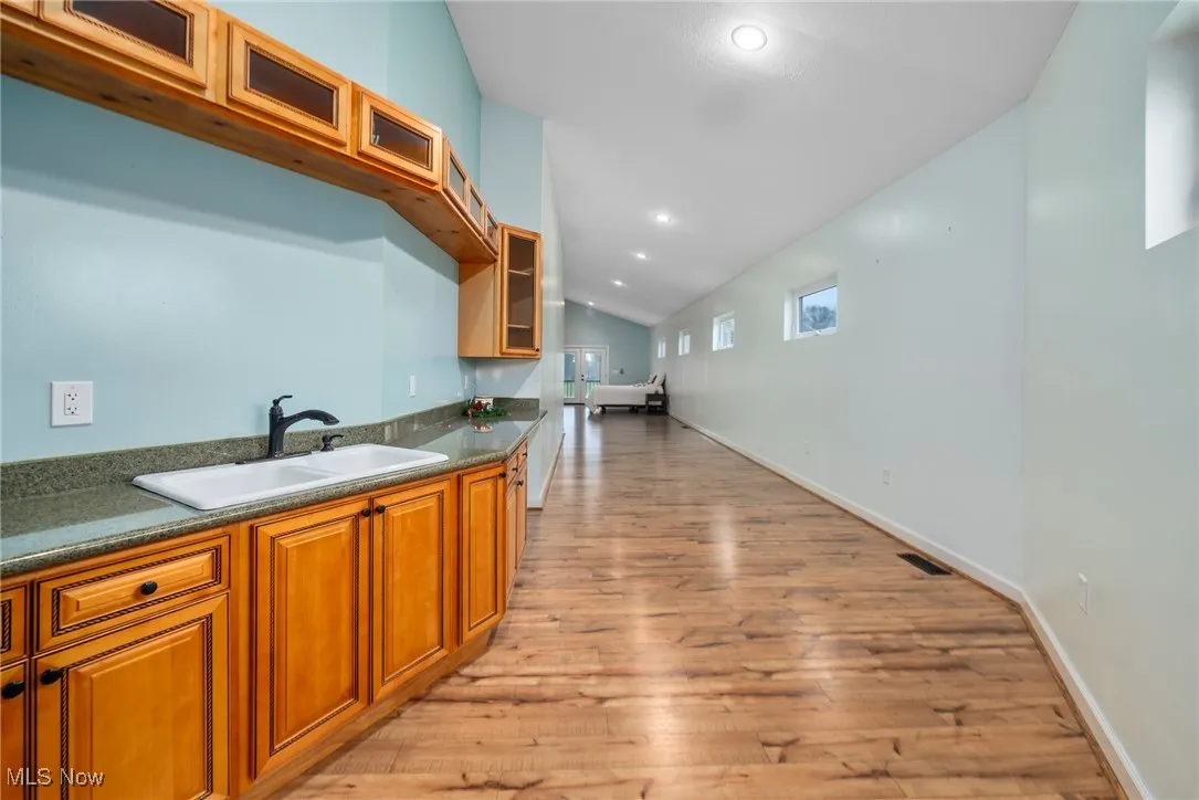 Kitchen with vaulted ceiling, glass insert cabinets, brown cabinets, light wood-style floors, and recessed lighting