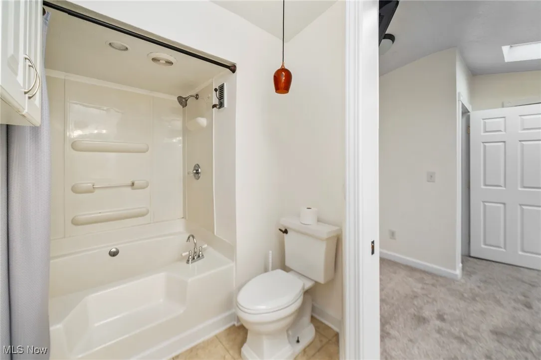 Full bathroom featuring shower / bath combination with curtain, light tile patterned flooring, a skylight, and light carpet