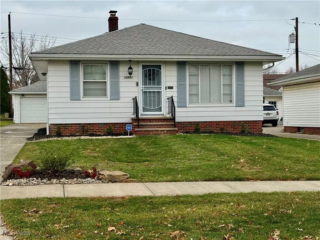 View of front of home with a shingled roof, a front lawn, a chimney, and a garage
