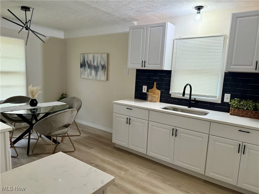 Kitchen with backsplash, a textured ceiling, light wood-style flooring, white cabinets, and light stone counters