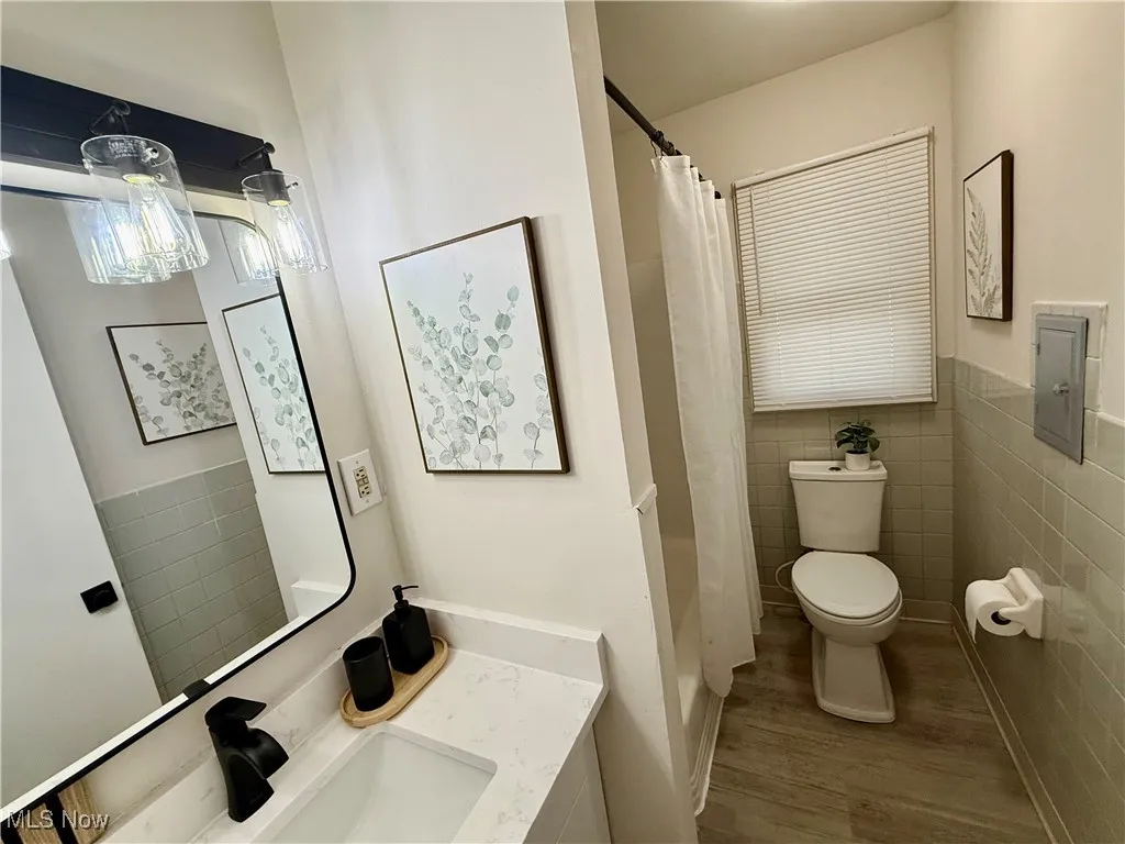 Bathroom featuring tile walls, vanity, wood finished floors, a wainscoted wall, and electric panel