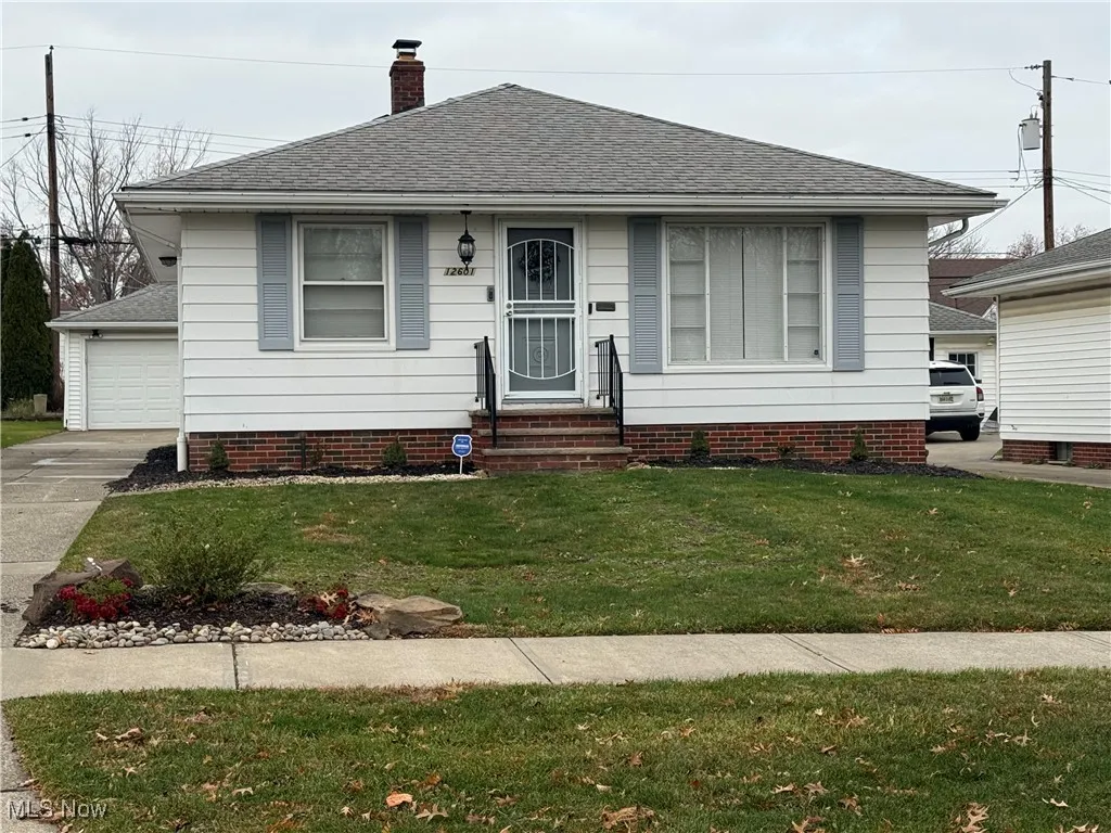 View of front of home with a shingled roof, a front lawn, a chimney, and a garage