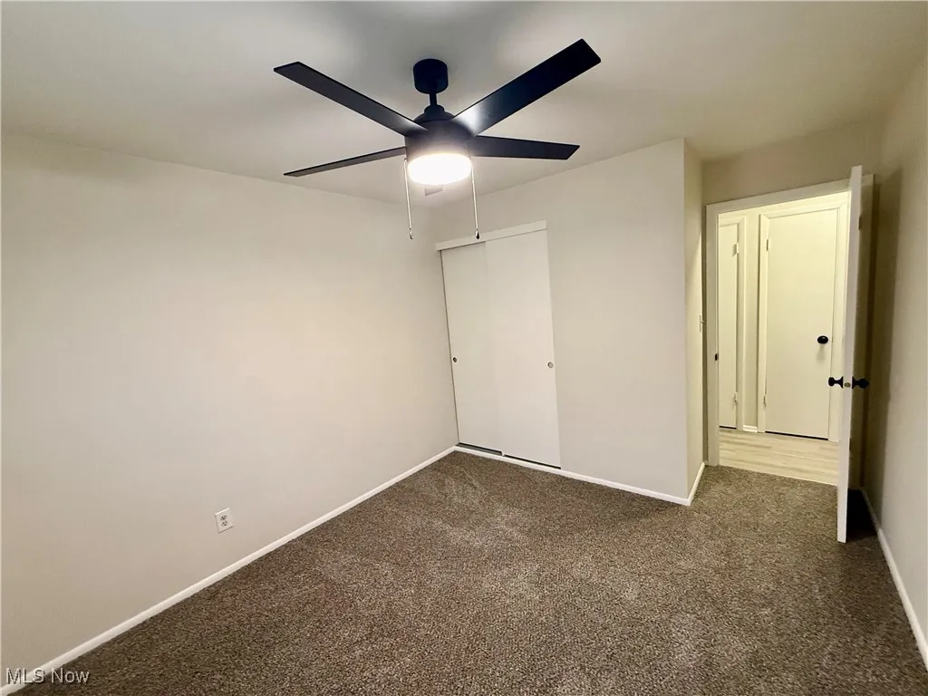 Unfurnished bedroom featuring dark colored carpet, ceiling fan, and a closet