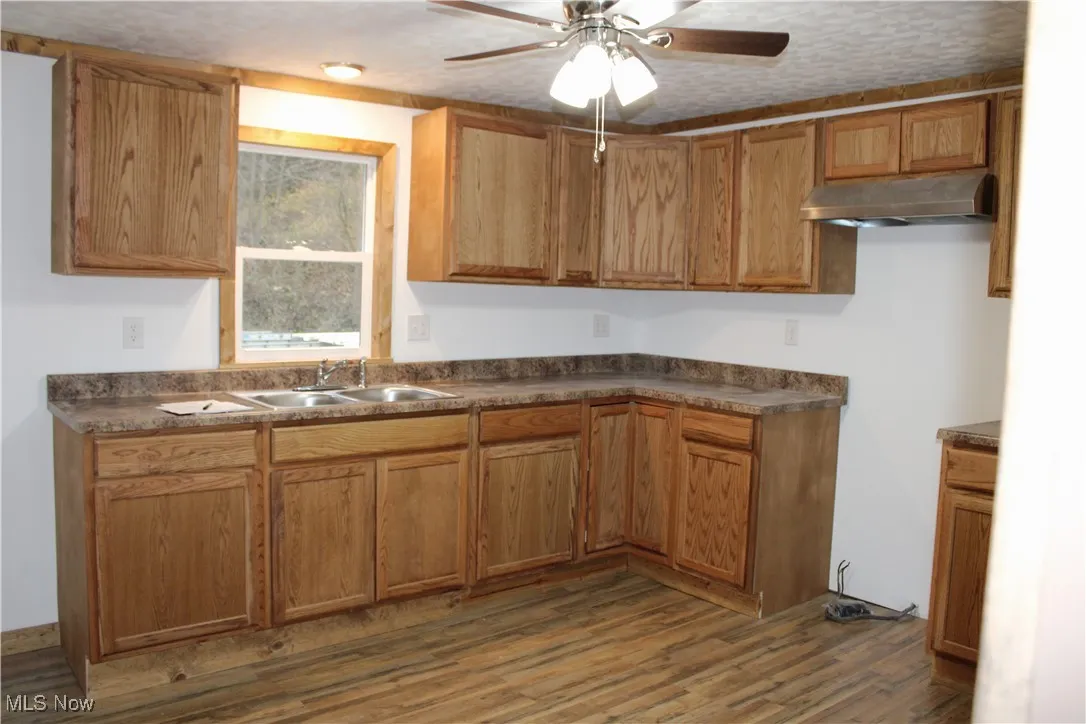Kitchen featuring dark countertops, ceiling fan, dark wood-style flooring, under cabinet range hood, and brown cabinetry