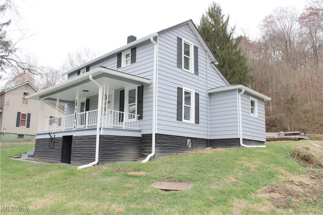 View of side of property featuring covered porch, a chimney, and a yard