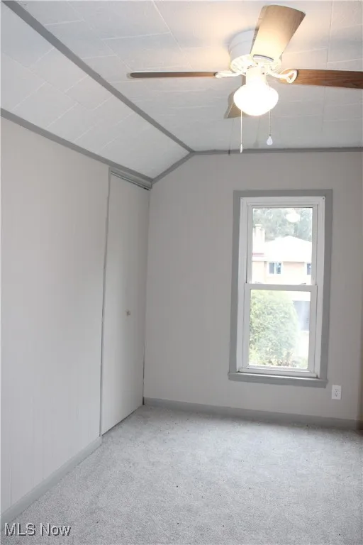 Carpeted empty room with wood walls, ceiling fan, and vaulted ceiling