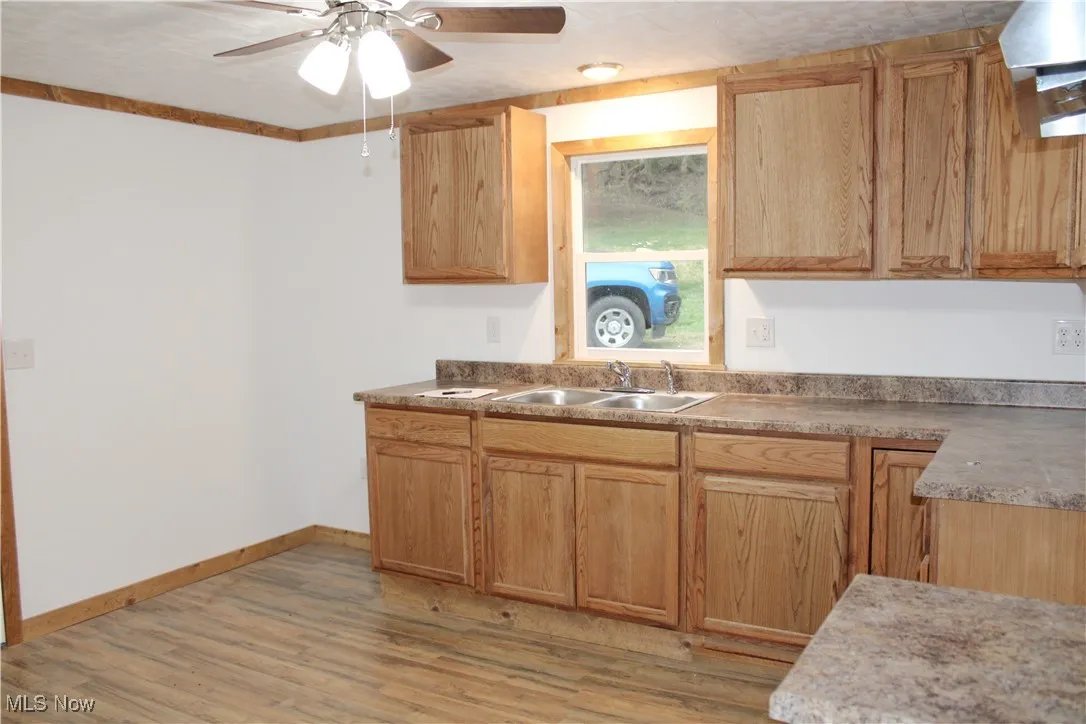 Kitchen featuring wall chimney exhaust hood, light wood-style flooring, light countertops, and a ceiling fan