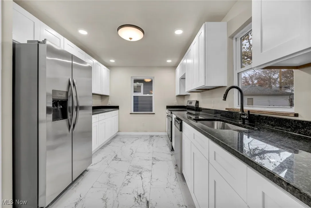 Kitchen with dark stone countertops, appliances with stainless steel finishes, recessed lighting, white cabinets, and light marble finish floors