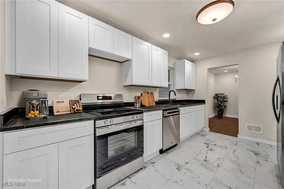 Kitchen featuring light marble finish floors, stainless steel appliances, dark countertops, white cabinetry, and recessed lighting