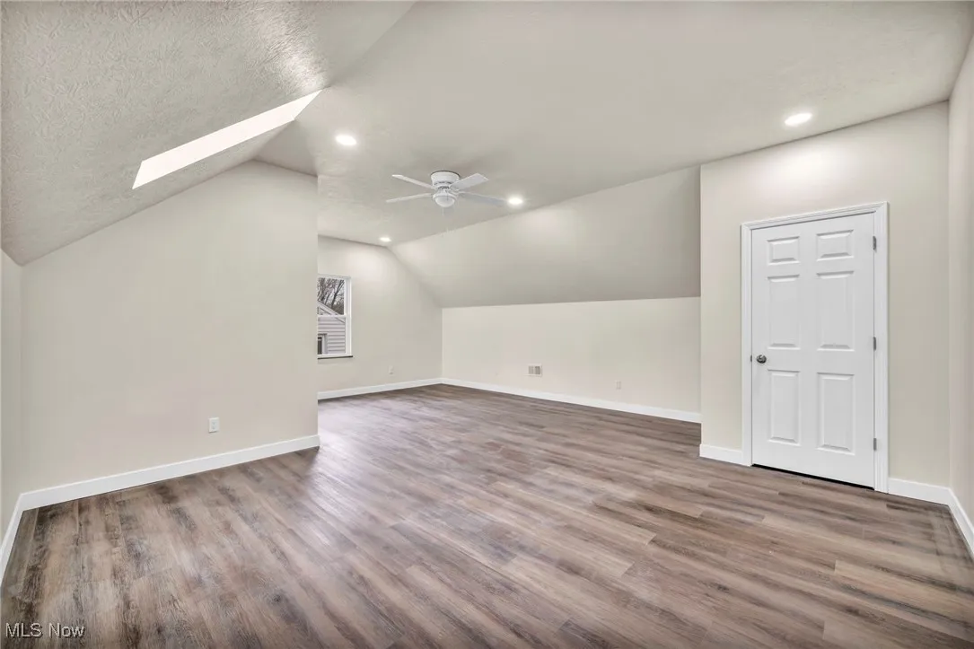 Additional living space featuring lofted ceiling, dark wood-type flooring, a skylight, recessed lighting, and ceiling fan
