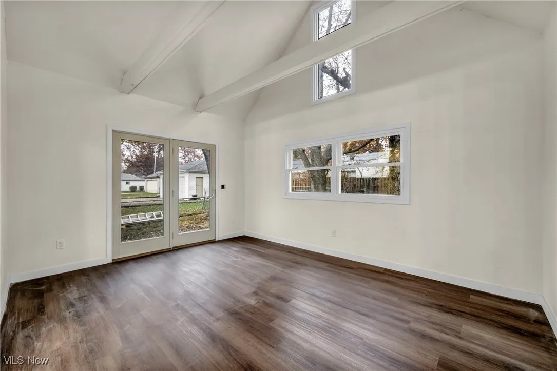 Unfurnished room featuring beam ceiling, high vaulted ceiling, dark wood finished floors, and healthy amount of natural light