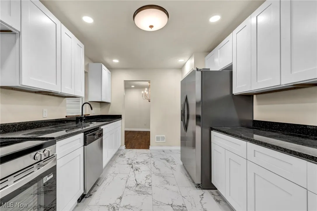 Kitchen featuring light marble finish flooring, recessed lighting, white cabinetry, dark stone countertops, and a chandelier