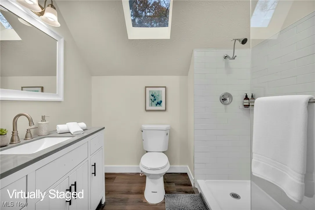 Full bathroom with a skylight, a textured ceiling, vanity, a tile shower, and dark wood finished floors