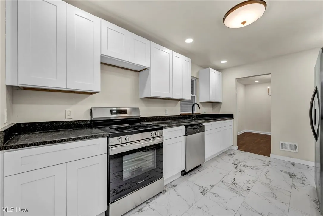 Kitchen featuring appliances with stainless steel finishes, light marble finish flooring, white cabinets, recessed lighting, and dark stone counters