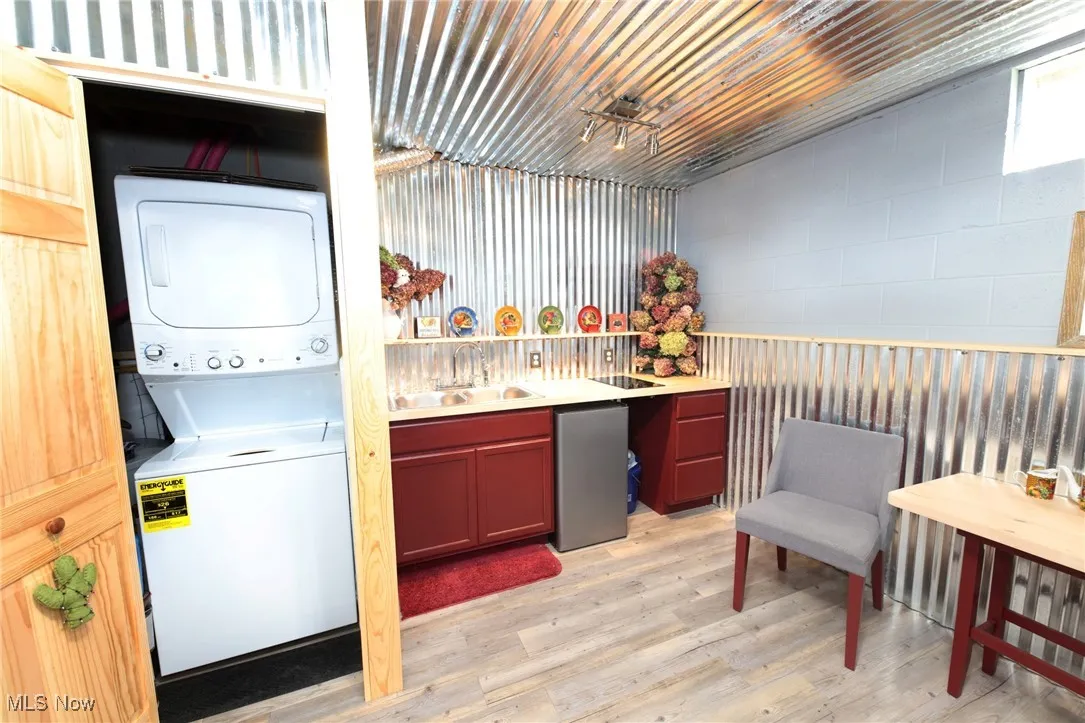 Laundry room with light wood-style flooring, estacked washer and dryer, and concrete block wall