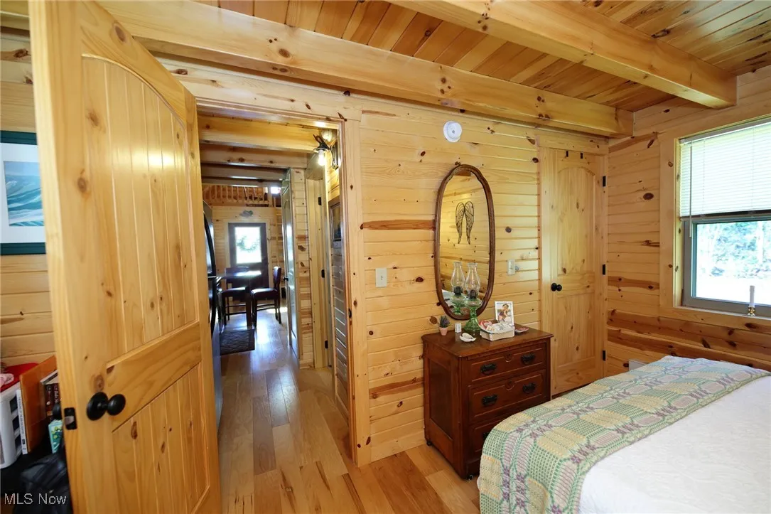 Bedroom featuring light wood-type flooring, a wood ceiling with exposed beams, and wooden walls