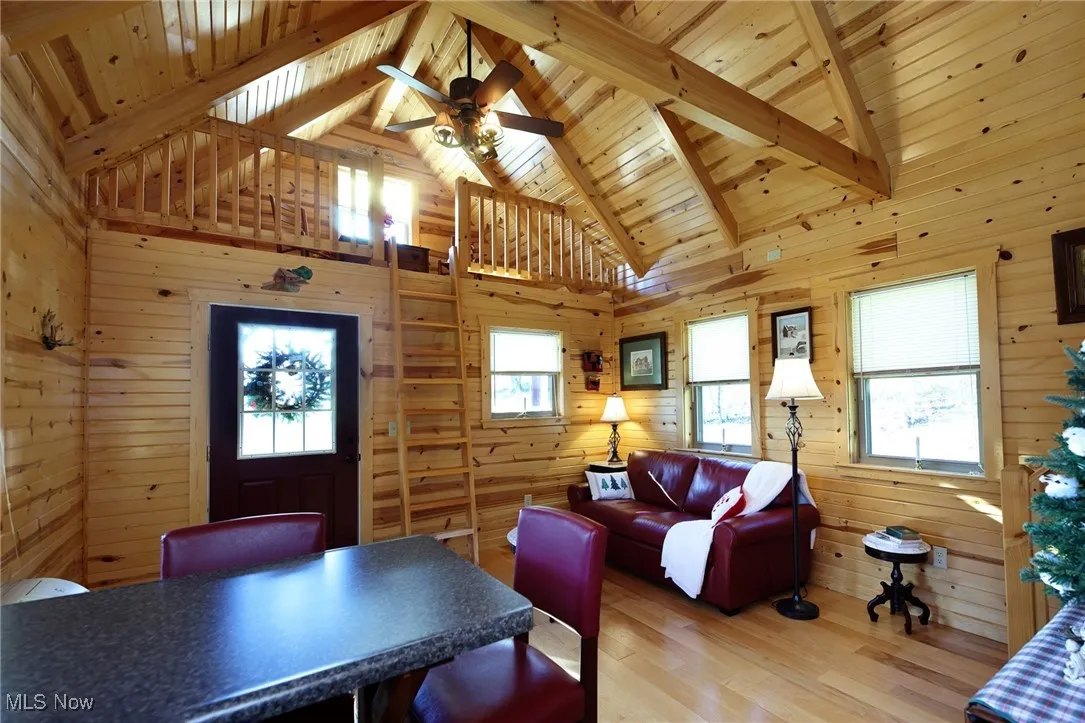Living area featuring wooden walls, high vaulted ceiling, light wood-style flooring, a wooden ceiling with exposed beams, and plenty of natural light