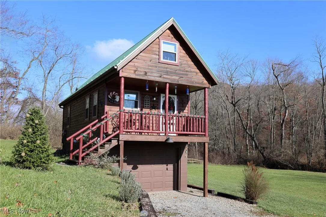 Chalet / cabin featuring an attached garage, a front lawn, a view of trees, and driveway