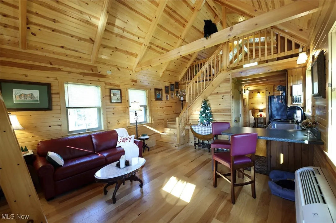 Living room with stairs, a wood ceiling with exposed beams, wood walls, high vaulted ceiling, and light wood finished floors