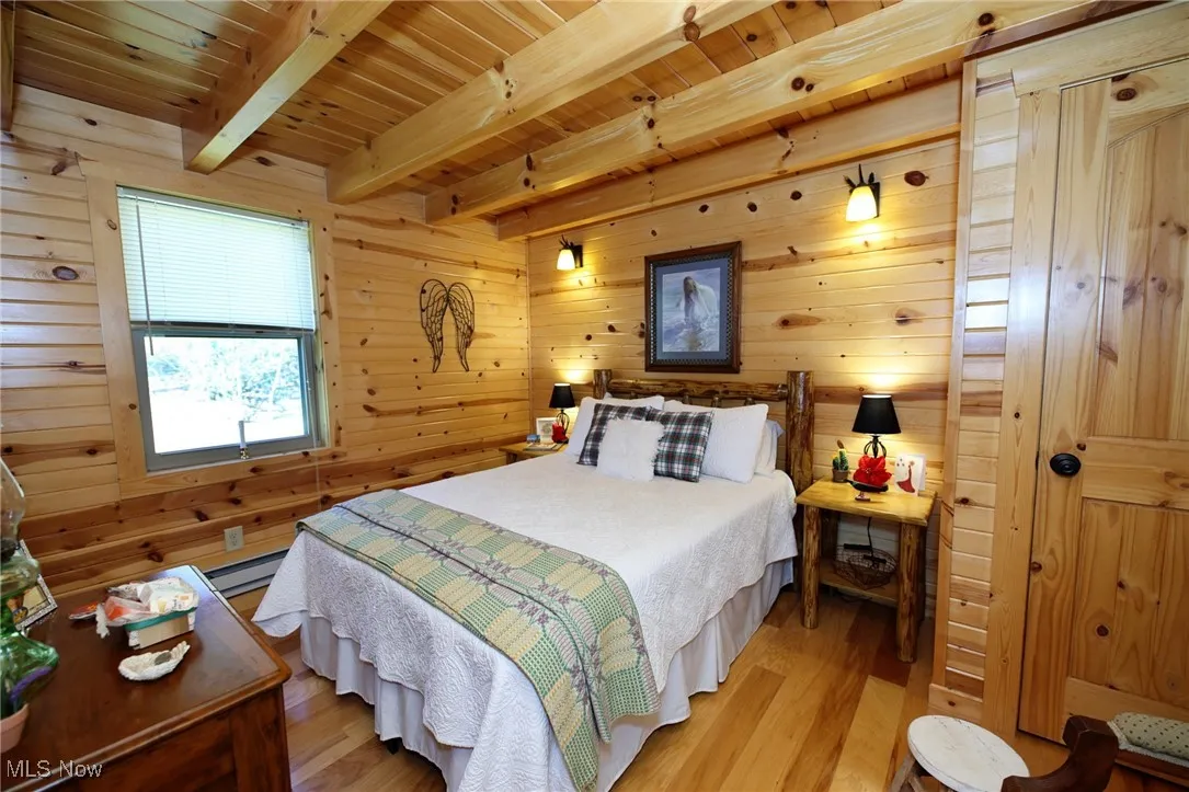 Bedroom featuring wood finished floors, a wooden ceiling with exposed beams, wood walls, and a baseboard heating unit