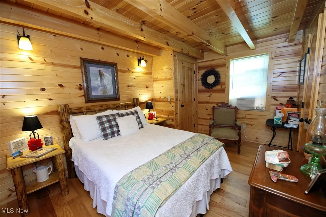 Bedroom featuring wood finished floors, wooden walls, and a wood ceiling with exposed beams
