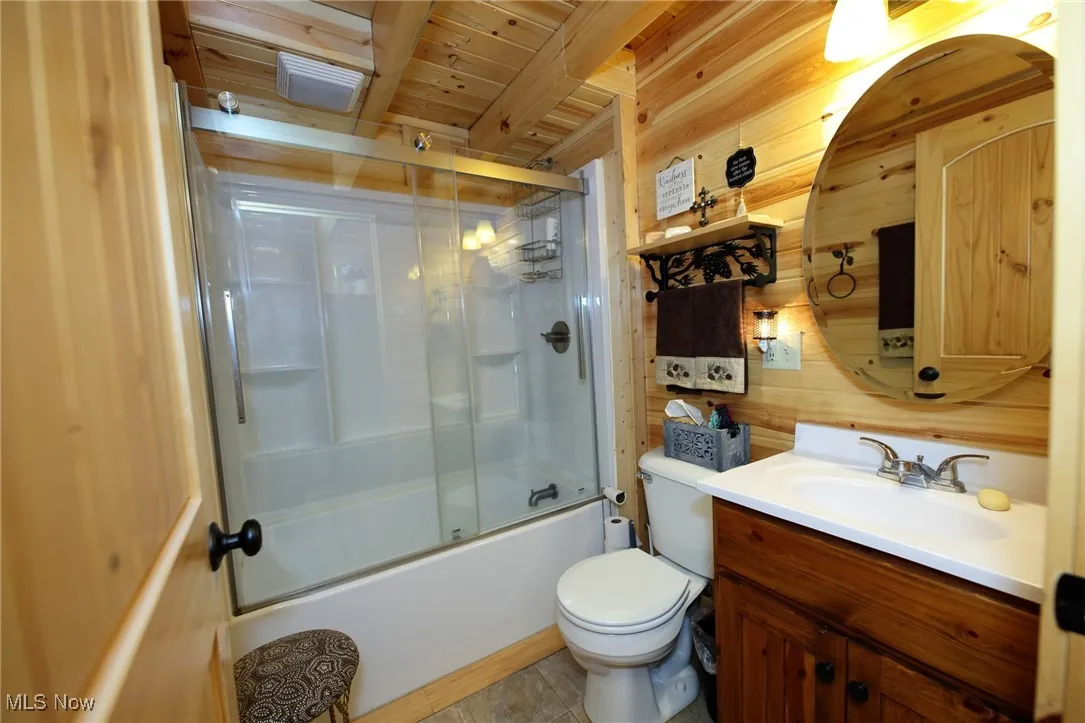 Full bath with wooden walls, combined bath / shower with glass door, vanity, and wooden ceiling