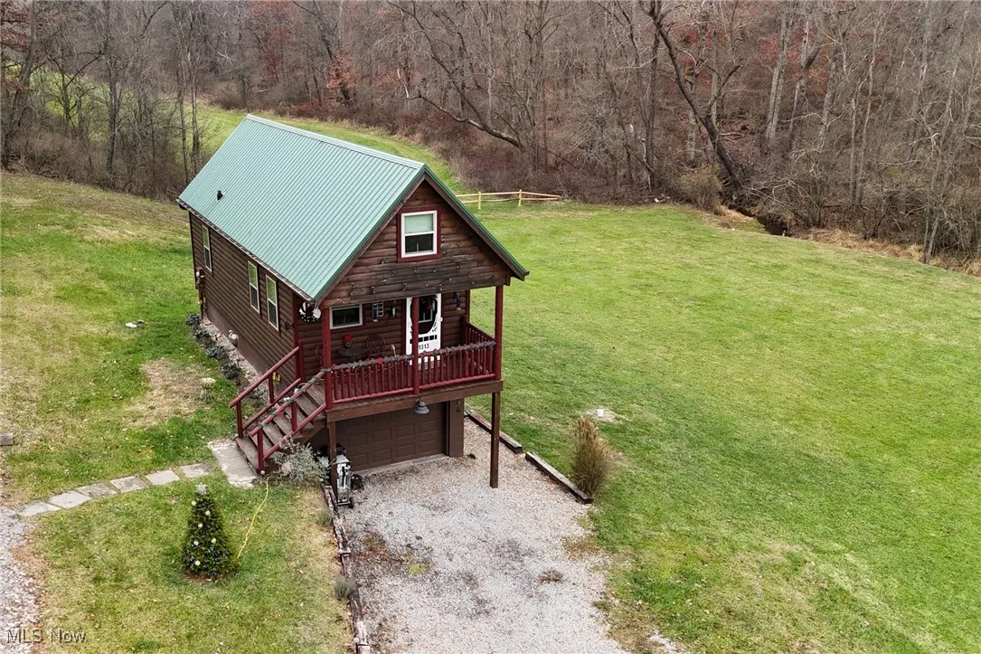 View of front of property with driveway, a wooden deck, a metal roof, and a front lawn