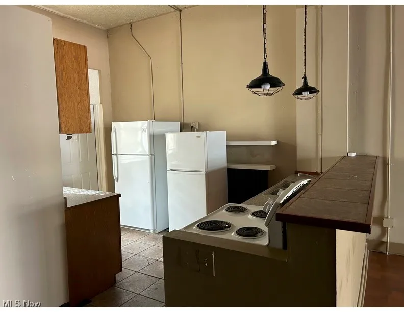 Kitchen with freestanding refrigerator, a peninsula, decorative light fixtures, dark tile patterned flooring, and a textured ceiling