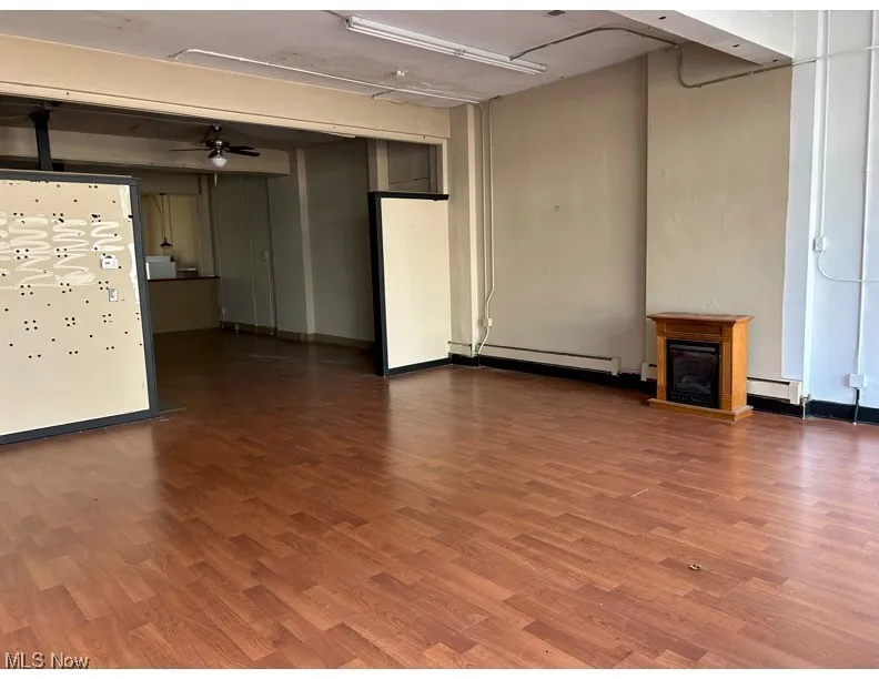 Unfurnished living room featuring a ceiling fan, a fireplace with raised hearth, wood finished floors, and baseboard heating