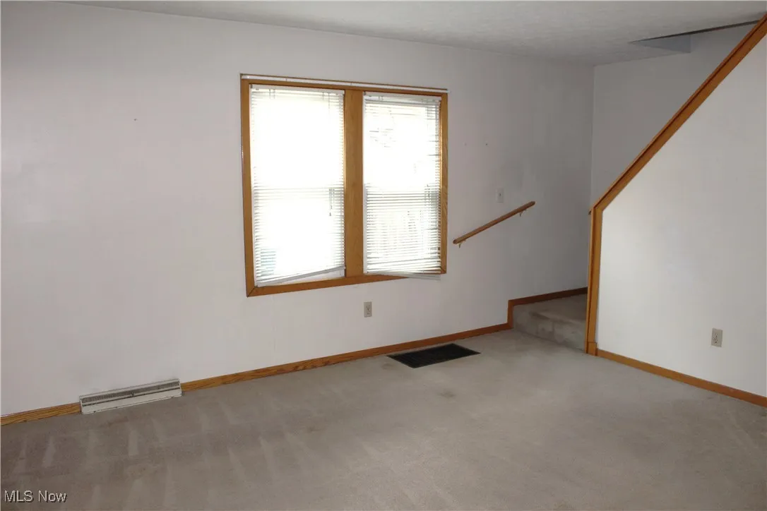 Unfurnished living room featuring light colored carpet and stairs