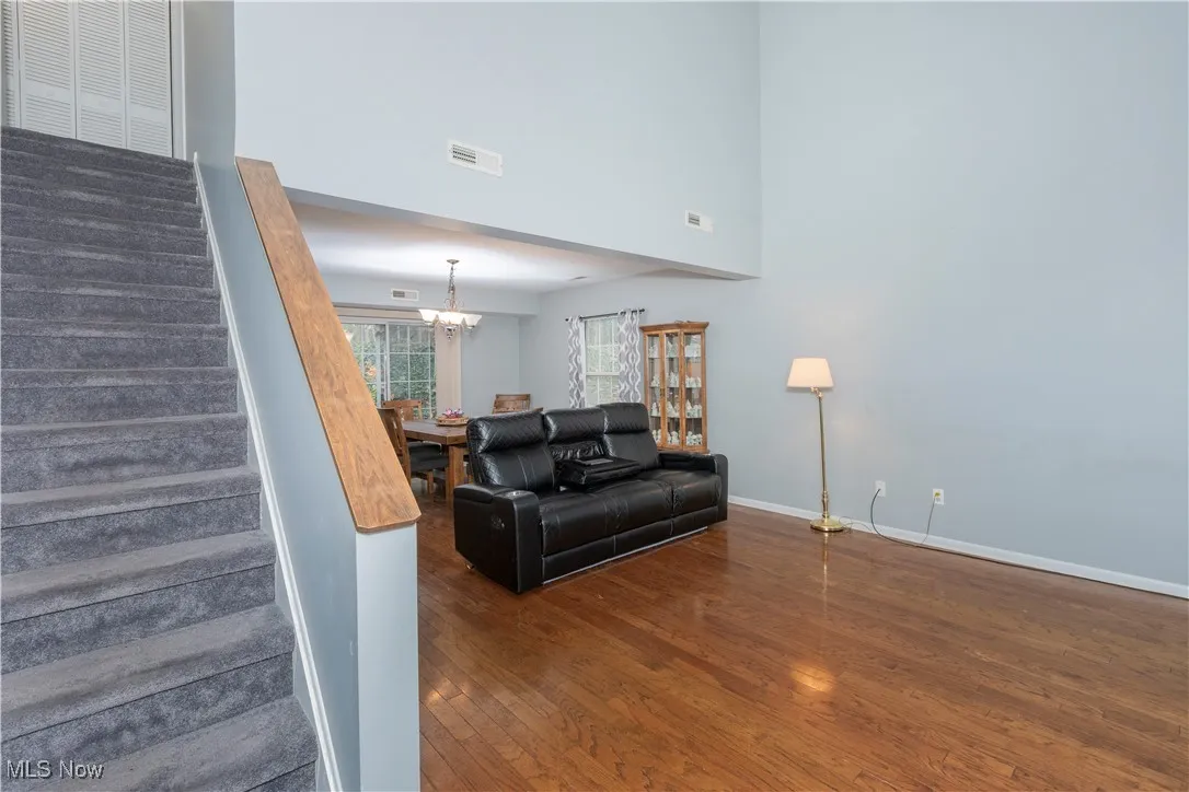 Living room featuring dark wood-style flooring, a high ceiling, a chandelier, and stairs
