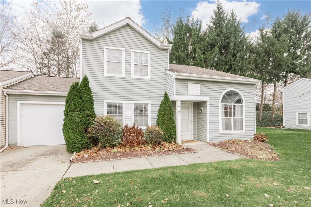 Traditional-style house with a front yard, roof with shingles, an attached garage, and driveway