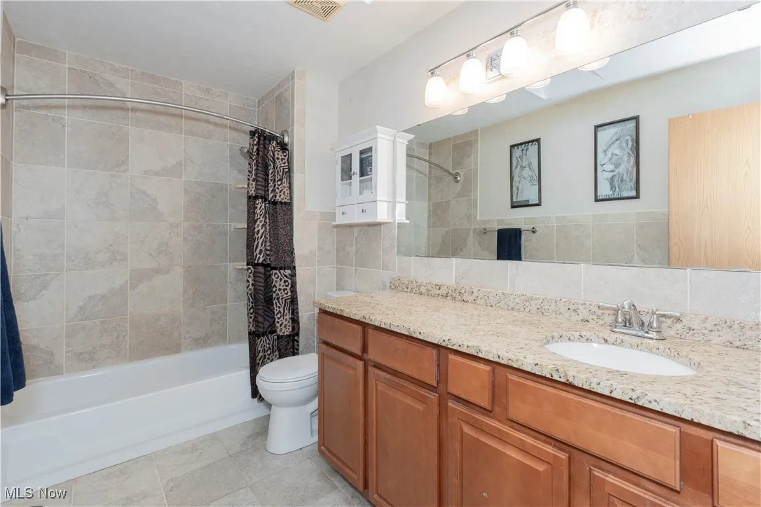 Full bath featuring vanity, shower / bath combo with shower curtain, tile walls, and light tile patterned flooring