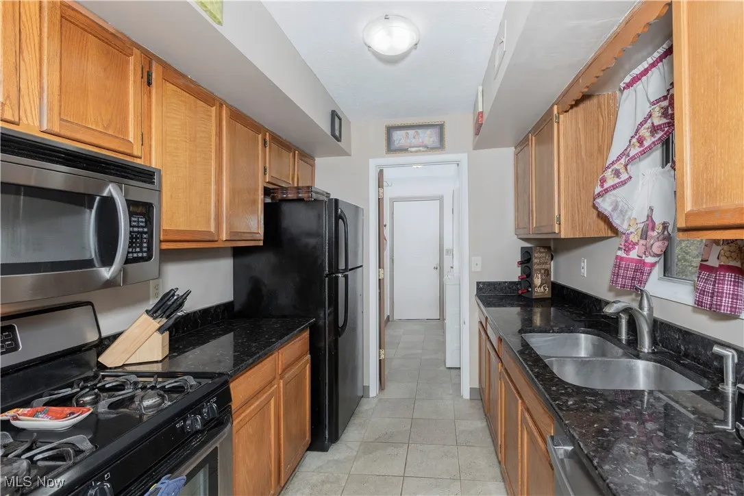 Kitchen featuring appliances with stainless steel finishes, dark stone counters, light tile patterned flooring, and brown cabinets